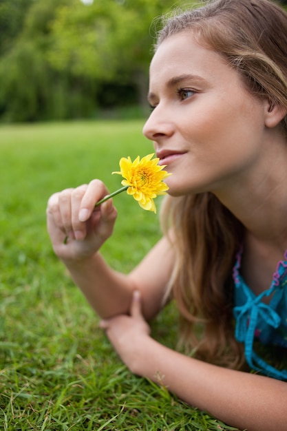 Jeune fille détendue, allongée sur l&#39;herbe dans la campagne tout en sentant une fleur