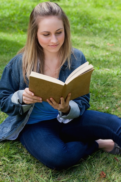 Jeune fille détendue, lire un livre tout en étant assis sur l&#39;herbe