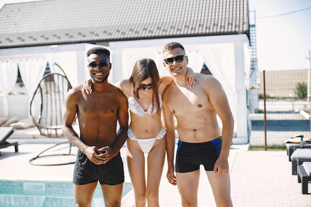 Jeune fille et deux de ses amis masculins multiraciaux debout sur une plage. Fille portant des maillots de bain blancs et des lunettes de soleil