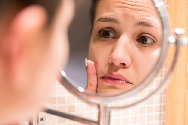 Jeune fille devant un miroir de salle de bain mettant de la crème sur un bouton rouge Beauté soins de la peau et bien-être matin concept