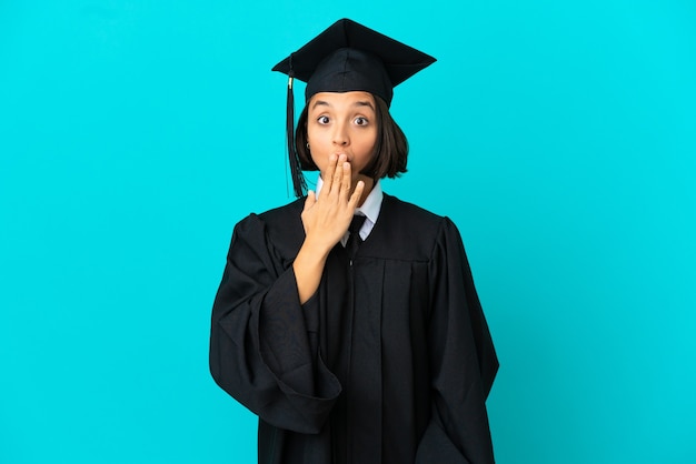 Jeune fille diplômée universitaire sur fond bleu isolé couvrant la bouche avec la main