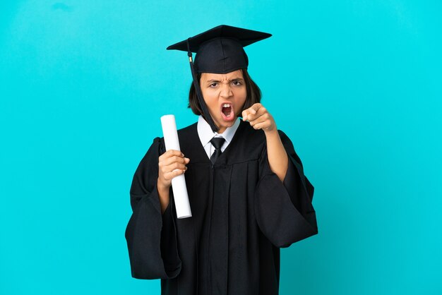 Jeune fille diplômée universitaire sur fond bleu isolé frustré et pointant vers l'avant