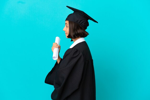 Jeune fille diplômée universitaire sur fond bleu isolé en position latérale