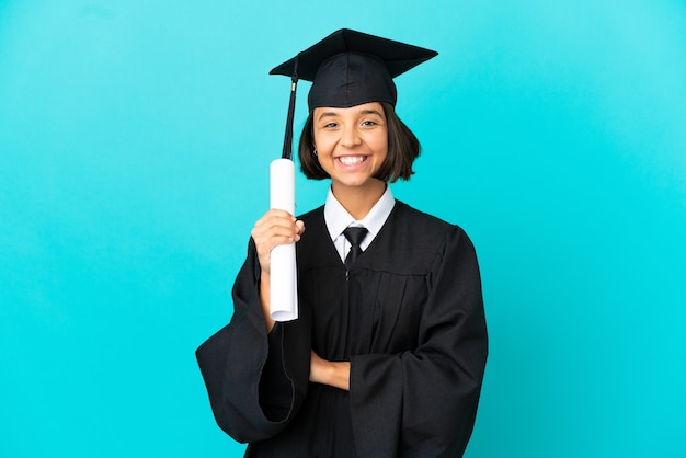 Jeune fille diplômée de l'université sur fond bleu isolé en gardant les bras croisés en position frontale