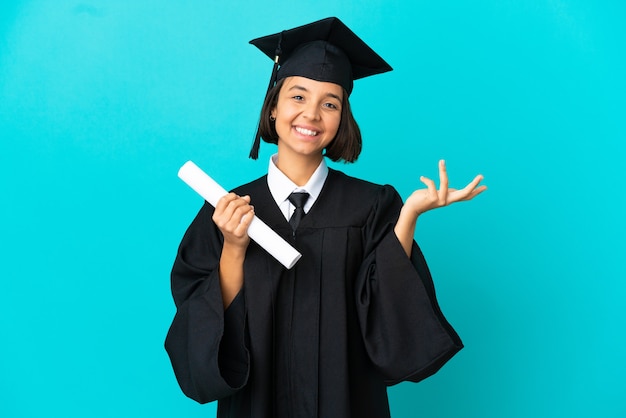 Jeune fille diplômée d'université sur fond bleu isolé tendant les mains sur le côté pour inviter à venir