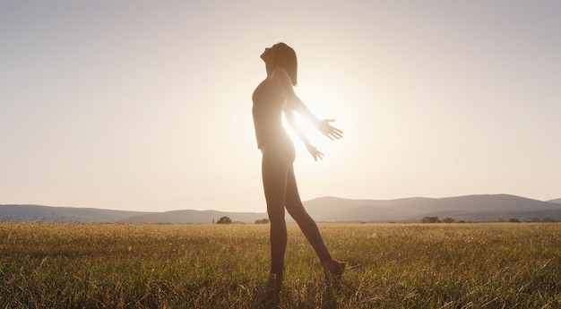 Jeune fille écartant les mains avec joie et inspiration face au soleil