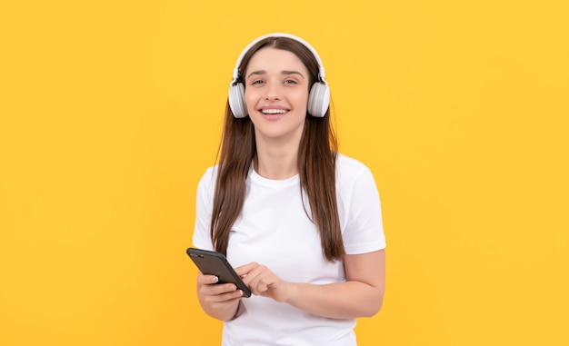 Jeune fille écouter de la musique dans les écouteurs tenir le téléphone sur la technologie de fond jaune