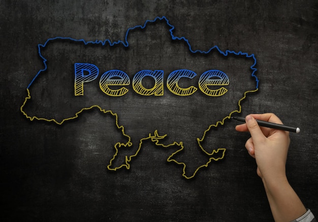 La jeune fille écrit sur le tableau noir le texte Paix sur la carte de l'Ukraine
