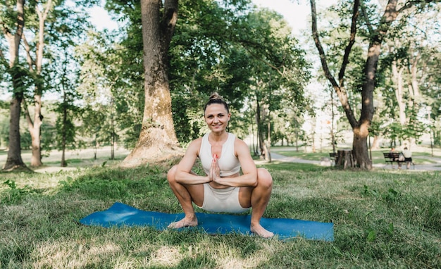 Une jeune fille effectue des exercices de yoga complexes dans le parc à l'extérieur