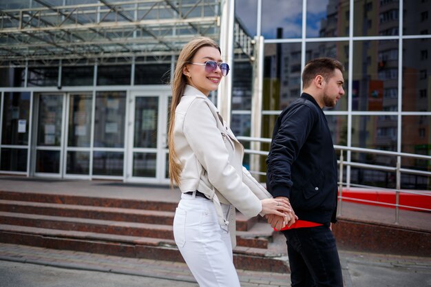 Jeune fille élégante aux cheveux blonds d'apparence européenne et un gars dans une veste noire. Promenade urbaine d'un couple amoureux, mode moderne dans un style décontracté. Concept de relation heureuse