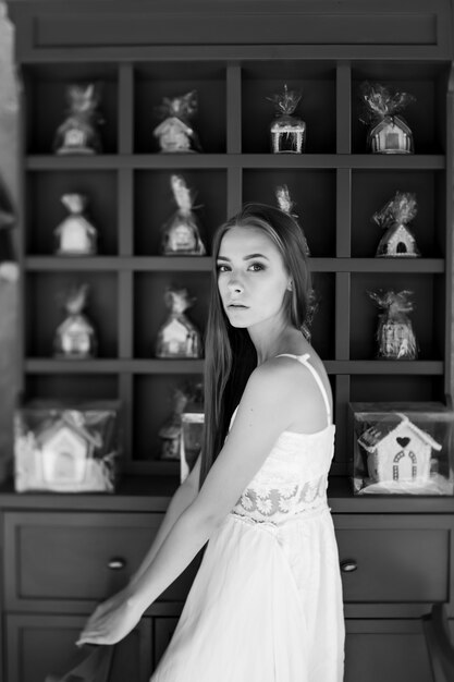 Jeune fille élégante en robe blanche posant sur un mur décoré