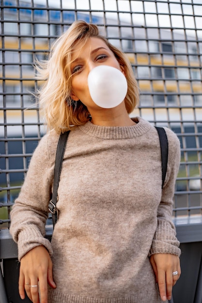 Jeune fille élégante urbaine. Portrait émotionnel à l'extérieur du modèle de femme active. Mode de vie sain. Look de mode, portrait de hipster en plein air. Portrait en gros plan d'une jolie jeune fille mâchant du chewing-gum.