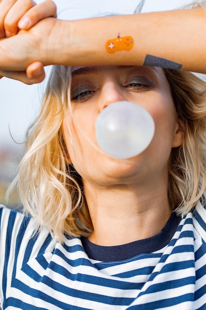 Jeune fille élégante urbaine. Portrait émotionnel à l'extérieur du modèle de femme active. Mode de vie sain. Look de mode, portrait de hipster en plein air. Portrait en gros plan d'une jolie jeune fille mâchant du chewing-gum.