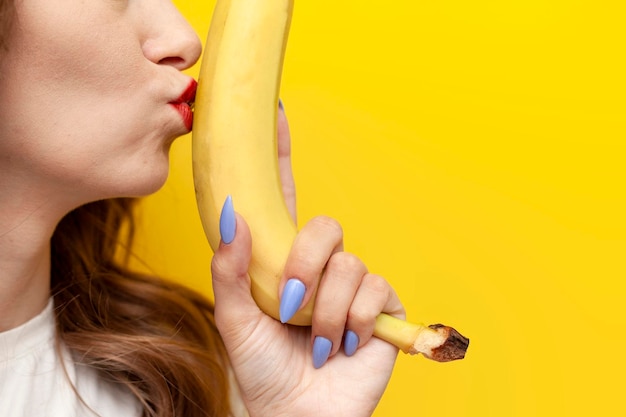 jeune fille embrasse la banane et fait allusion à l'intimité sur fond jaune isolé concept sexy et érotique