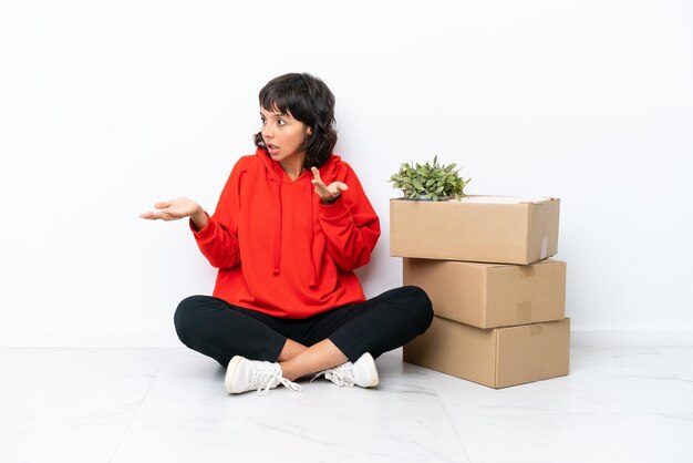 Jeune fille emménageant dans une nouvelle maison parmi des boîtes isolées sur fond blanc avec une expression faciale surprise