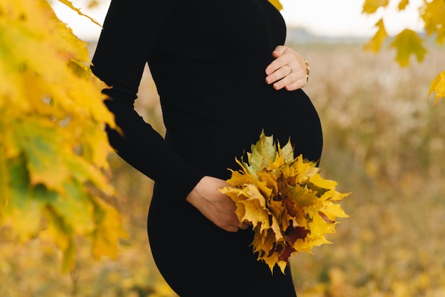 Jeune fille enceinte en automne feuilles jaunes bouchent le ventre