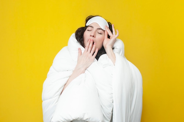 Photo jeune fille endormie dans un masque de sommeil et avec une couverture chaude et douce et confortable bâille