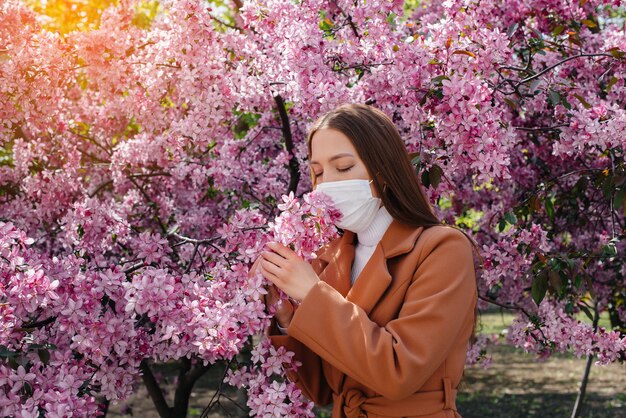 Une jeune fille enlève son masque et respire profondément après la fin de la pandémie un jour de printemps ensoleillé, devant des jardins fleuris. Protection et prévention covid 19.