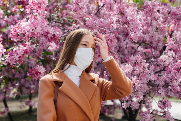 Une jeune fille enlève son masque et respire profondément après la fin de la pandémie un jour de printemps ensoleillé, devant des jardins fleuris. Protection et prévention covid 19.