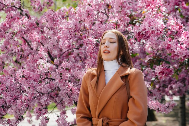 Une jeune fille enlève son masque et respire profondément après la fin de la pandémie un jour de printemps ensoleillé, devant des jardins fleuris.