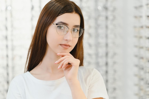Jeune fille essayant des lunettes devant un miroir Aider à améliorer la vision en sauvant la santé des yeux Debout près d'un support transparent avec des lentilles optiques