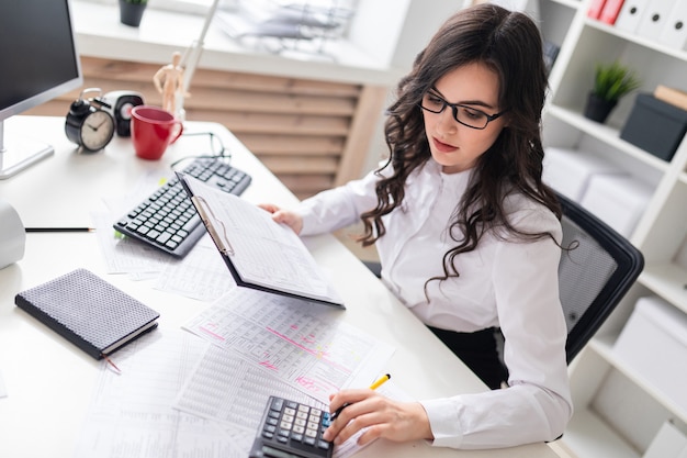 Une jeune fille est assise au bureau et bénit la calculatrice.