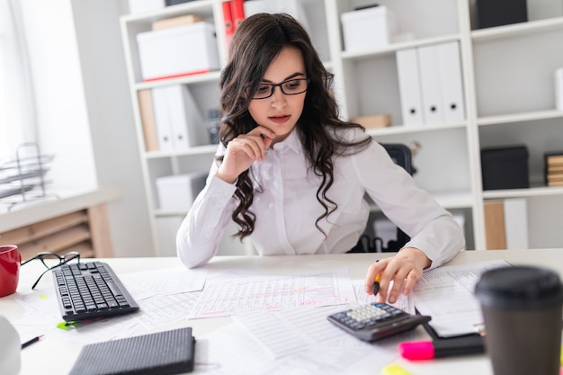 Une jeune fille est assise au bureau et bénit sur la calculatrice.