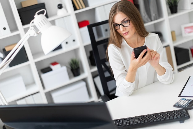 Une jeune fille est assise au bureau du bureau et tient un téléphone.