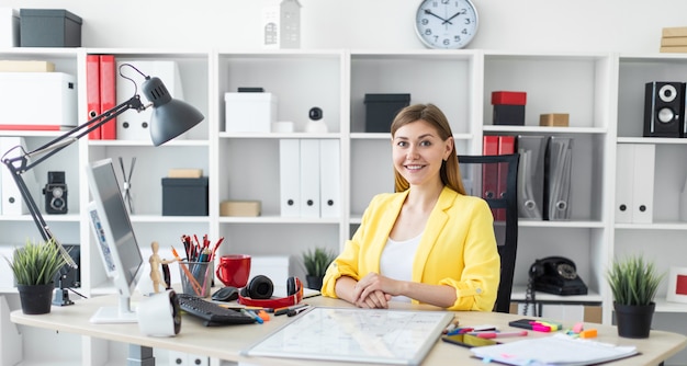 Une jeune fille est assise au bureau de l'ordinateur. Avant la fille, la table est un tableau magnétique.