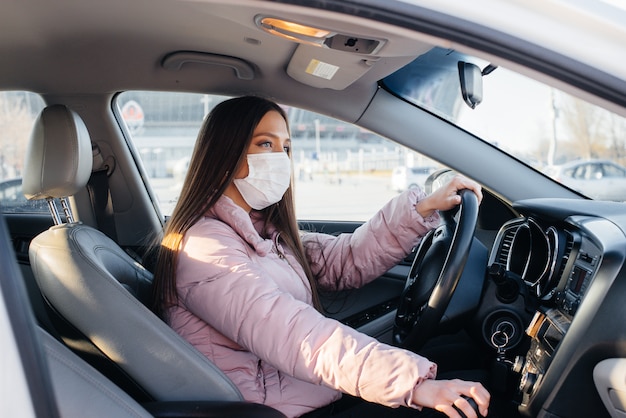 Une jeune fille est assise au volant de la voiture dans le masque pendant la pandémie mondiale et le coronavirus. Quarantaine.