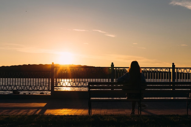 La jeune fille est assise sur un banc au bord d'un lac et admire