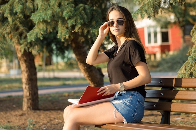 Une jeune fille est assise sur un banc dans un parc et prend des notes Vêtue d'une femme d'affaires de style libre parlant au téléphone avec des clients