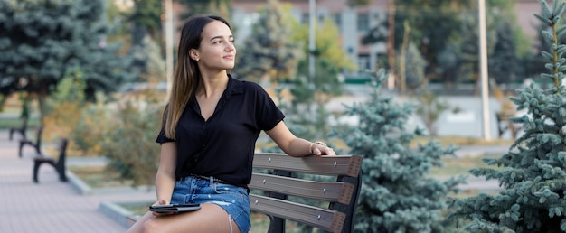 Une jeune fille est assise sur un banc dans un parc et prend des notes Vêtue d'une femme d'affaires de style libre parlant au téléphone avec des clients