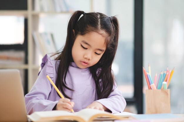 Une jeune fille est assise à un bureau avec un livre et un ordinateur portable