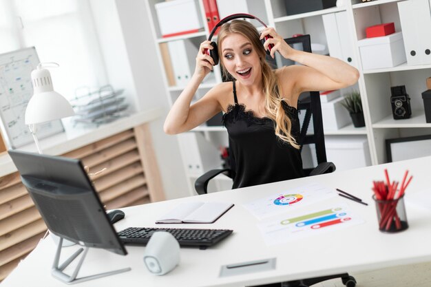 Une jeune fille est assise à un bureau d'ordinateur dans le bureau et met des écouteurs.