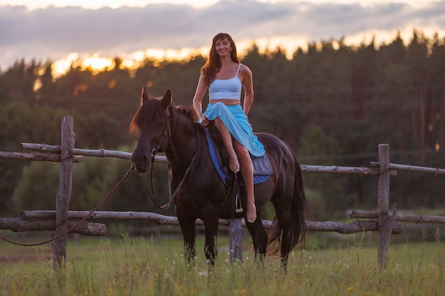 Photo une jeune fille est assise sur un cheval sur fond de forêt au coucher du soleil.