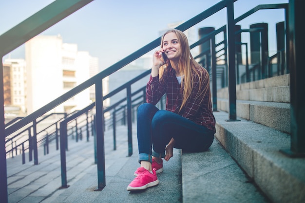 La jeune fille est assise sur les marches et parle au téléphone