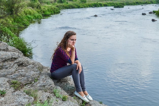 une jeune fille est assise sur un rocher près de la rivière