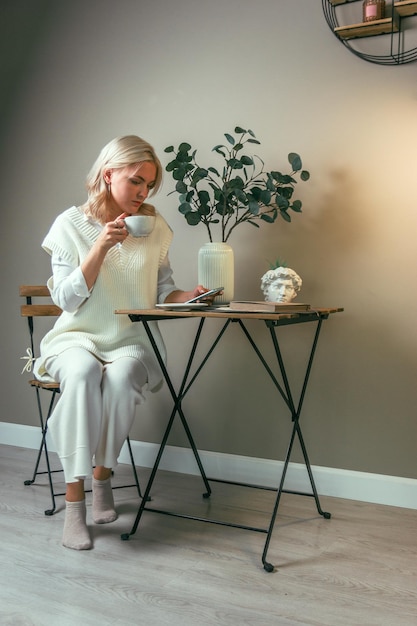 Une jeune fille est assise à une table basse avec un téléphone et une tasse de café dans les mains