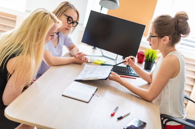 Une jeune fille est assise à une table dans son bureau et parle à deux co-partenaires.