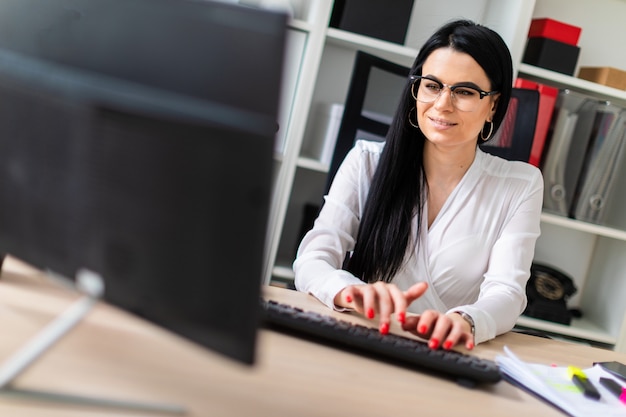 Une jeune fille est assise à la table et tape du texte sur le clavier