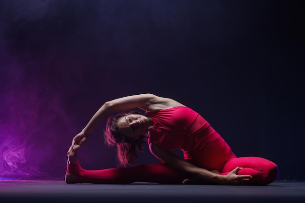 La jeune fille est engagée dans l'étirement sur un fond sombre une photo élégante de fitness et de yoga