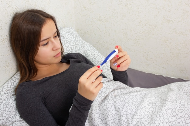 Une jeune fille est malade à la maison au lit, tient un thermomètre.