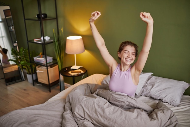 Jeune fille étirant ses bras et souriant en se réveillant le matin au lit à la maison