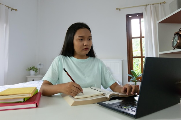 Jeune fille étudiant avec un ordinateur portable dans la chambre à coucher à la maison