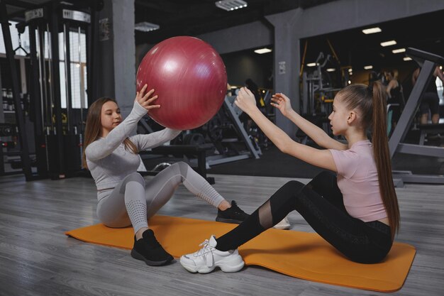 Jeune fille faisant de l'exercice avec son entraîneur personnel à l'aide d'un ballon en forme faisant de l'exercice pour les abdominaux