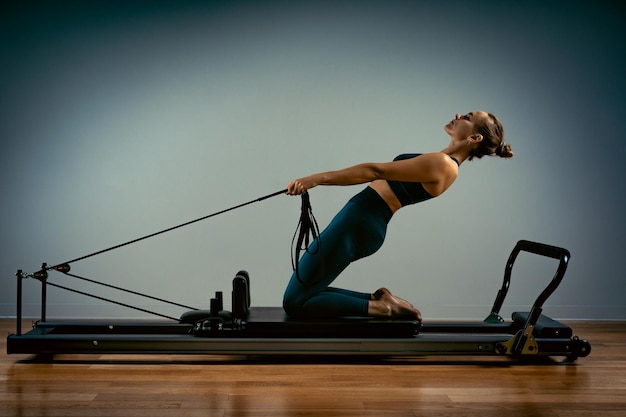 Jeune fille faisant des exercices de pilates avec un lit réformateur belle entraîneur de fitness mince sur réformateur