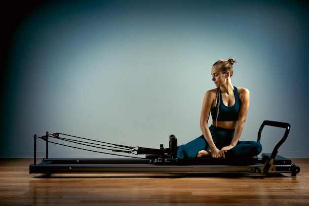 Jeune fille faisant des exercices de pilates avec un lit réformateur belle entraîneur de fitness mince sur réformateur