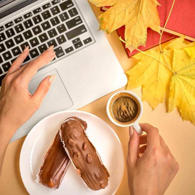 La jeune fille fait une pause-café sur le lieu de travail. Profiteroles à la crème avec une tasse de café et un ordinateur portable.