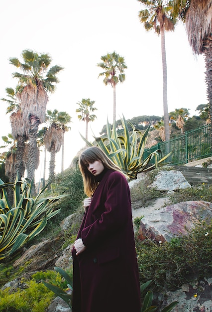 Jeune fille fashion dans un manteau violet dans les montagnes au milieu des paumes